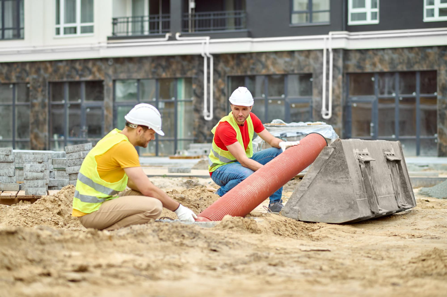 two-men-crouched-near-pipe-construction-site